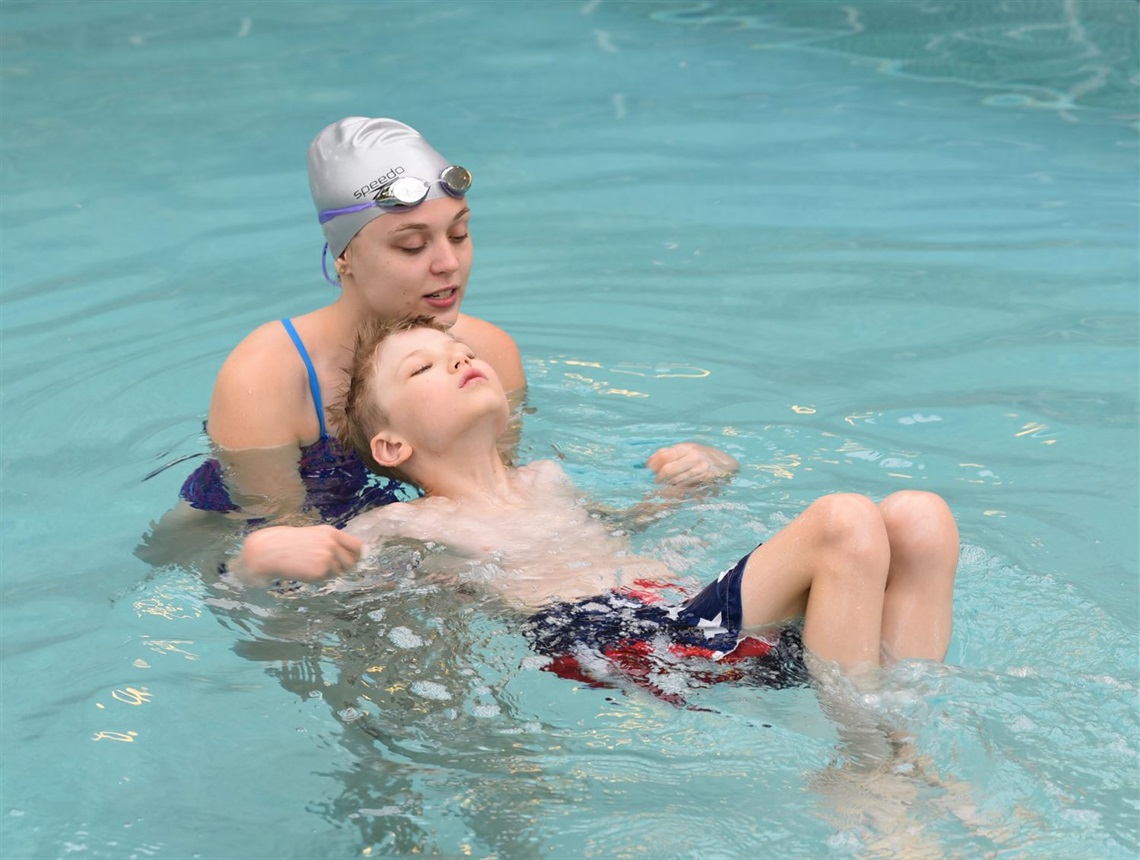 Female swim instructor steadying boy floating on his back